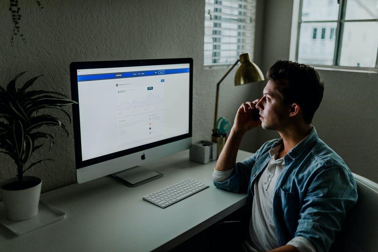 a man sitting and talking on the phone by looking at his computer about the revenue he have had