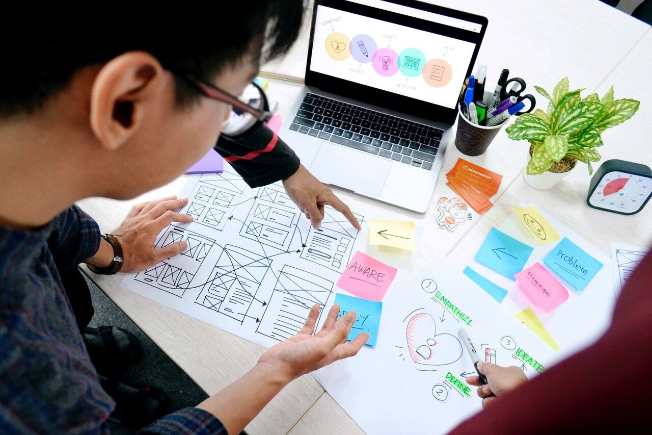 people discussing the best way to create with stick note papers and a laptop, pencil box, plant, and clock on the table